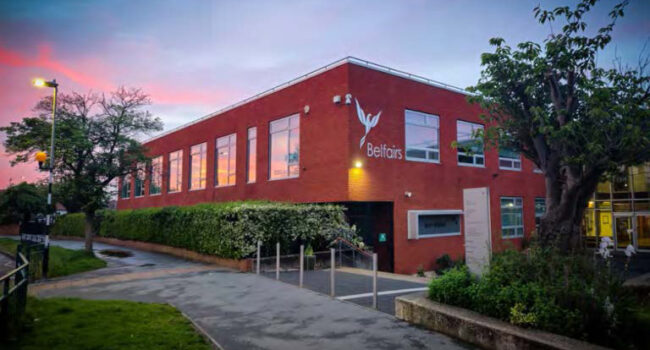 Belfairs Academy school building exterior at dusk, showing the red brick structure and entrance - welcoming families and students to the academy